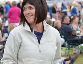 Close up of Gayle Goodwin carrying two drinks across a field
