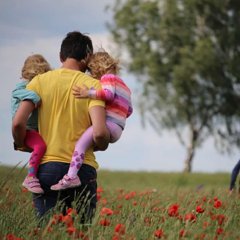 Father carrying two children in a field of poppies