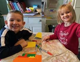Two children smiling at the camera while doing crafts and painting