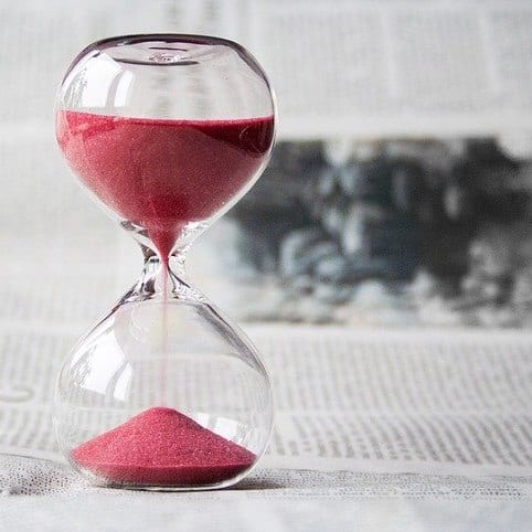 An hourglass with red sand placed on a newspaper