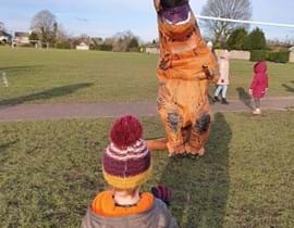 Man dressed as a dinosaur entertaining child in park