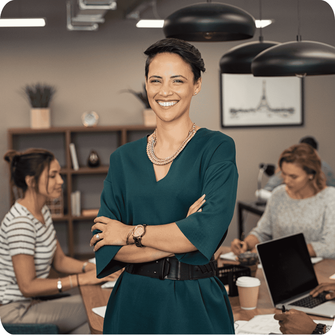 Business woman faces smiling at camera with female employees in the background in an office
